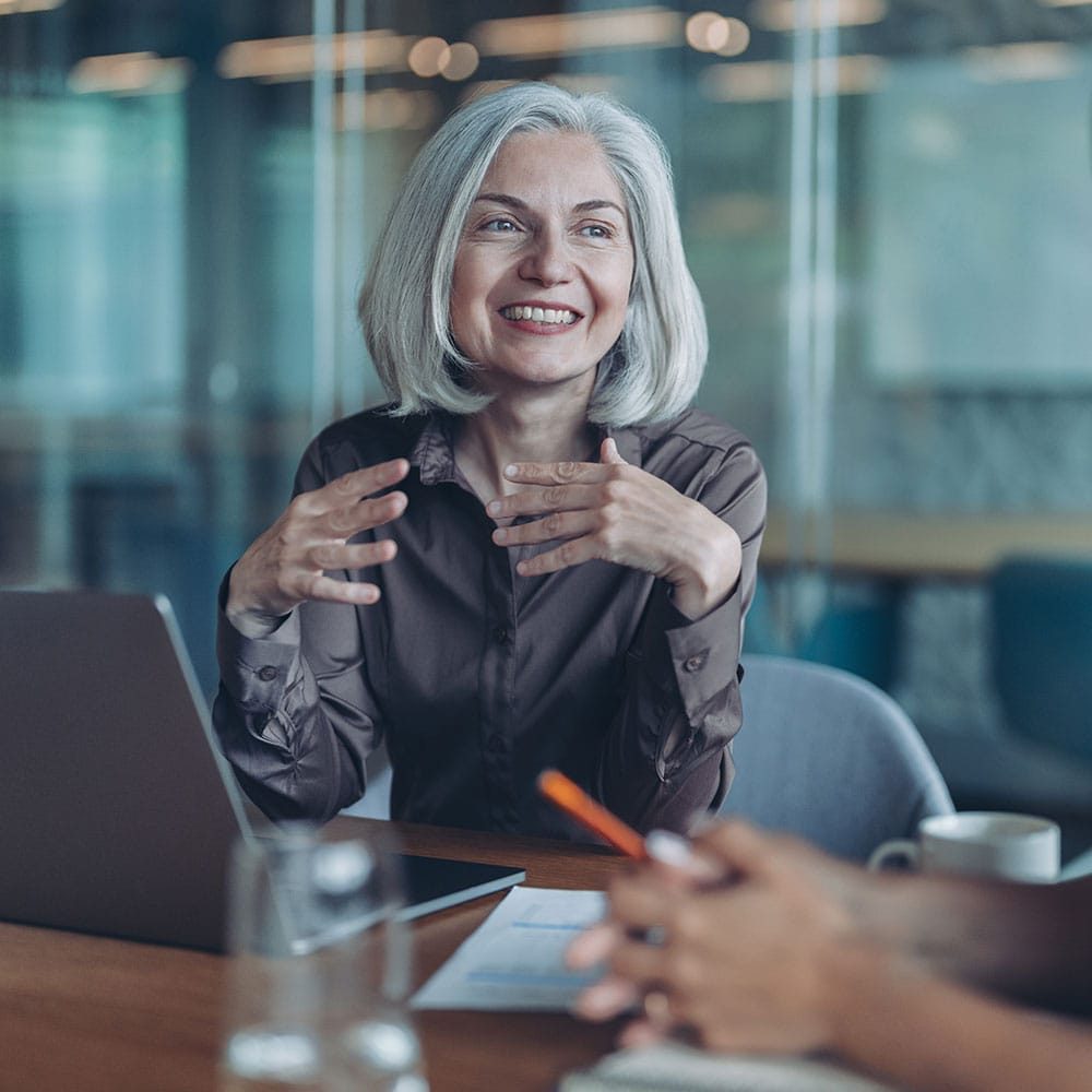 Professional woman smiling during a business meeting, engaging in conversation with colleagues in a modern office setting.