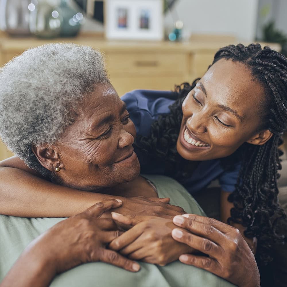 Caring young woman embracing elderly woman, symbolizing trust and estate support, in a warm, home setting.
